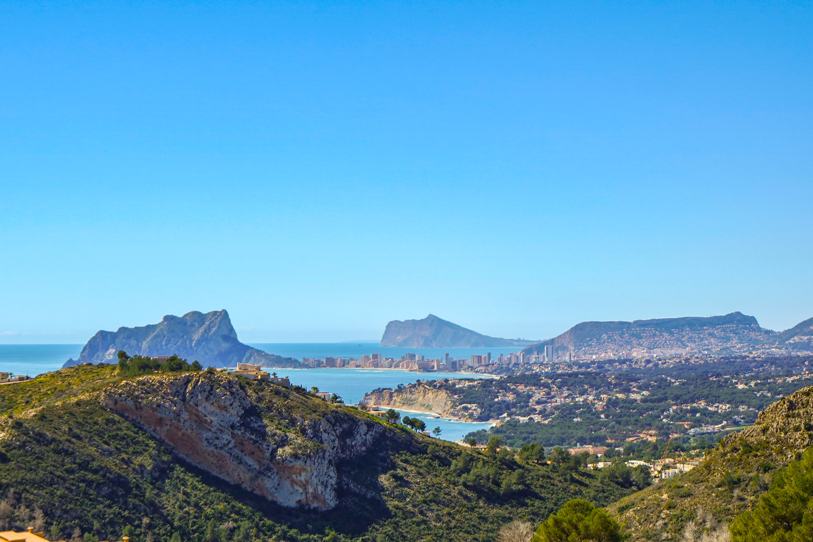 Panoramisch uitzicht vanaf de woning op de Peñón de Ifach in Calpe, de kustlijn van Benissa en de skyline van Benidorm in de verte bij een heldere hemel.