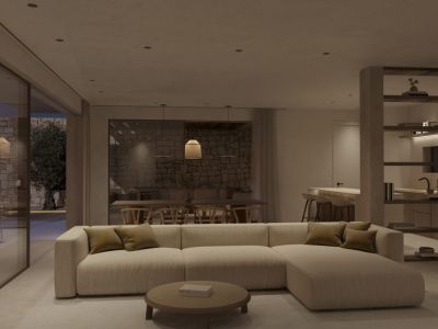 Open woon- en eetruimte met modulaire bank, ronde salontafel en schuifdeuren naar een stenen terras met olijfboom. Geïntegreerde keuken zichtbaar op de achtergrond.