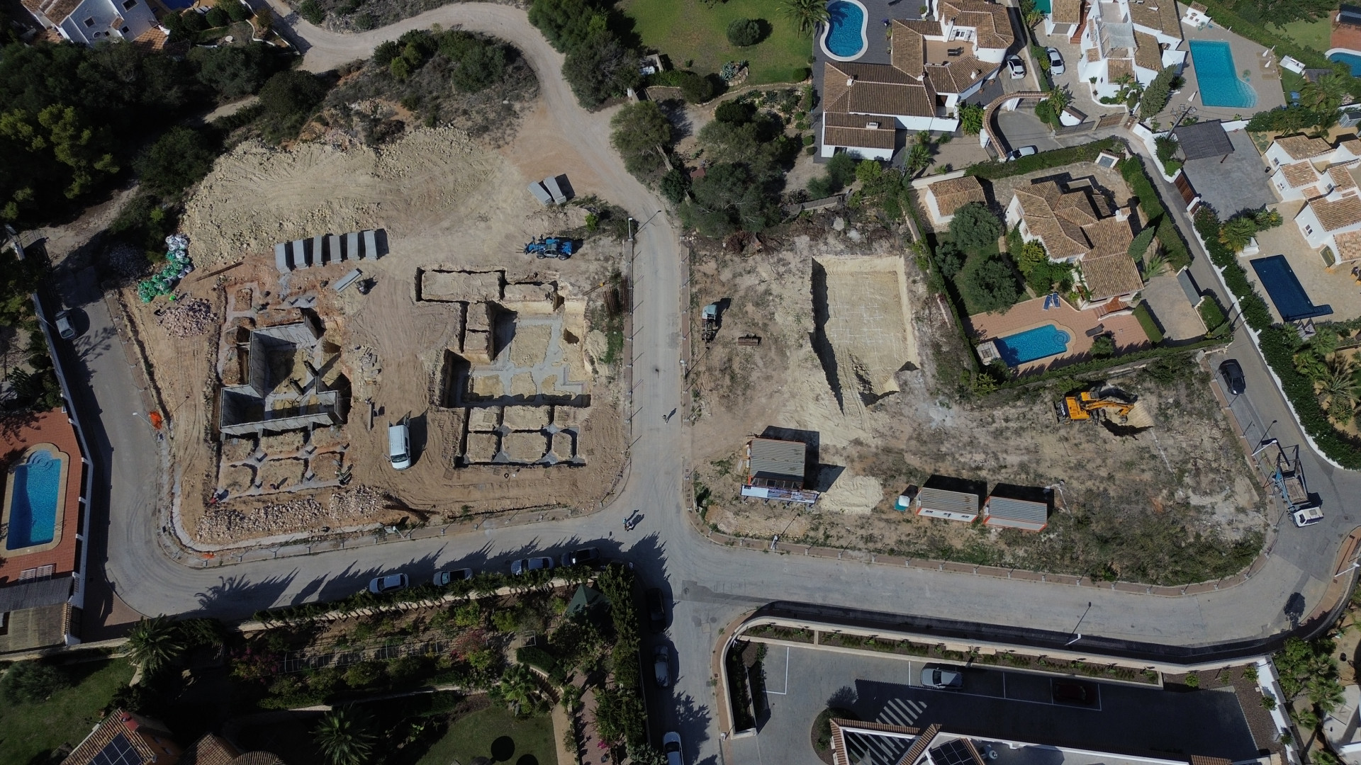 Luchtfoto van een residentieel bouwterrein in Jávea, met betonnen funderingen en uitgegraven percelen naast bestaande woningen met privézwembaden.