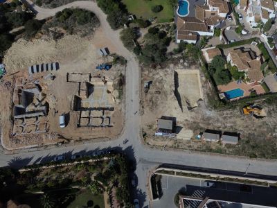 Luchtfoto van een residentieel bouwterrein in Jávea, met betonnen funderingen en uitgegraven percelen naast bestaande woningen met privézwembaden.