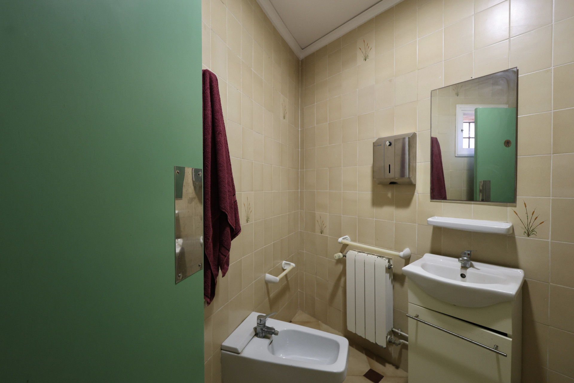 Badkamer met crèmekleurige tegels, een wit bidet en een groene deur.