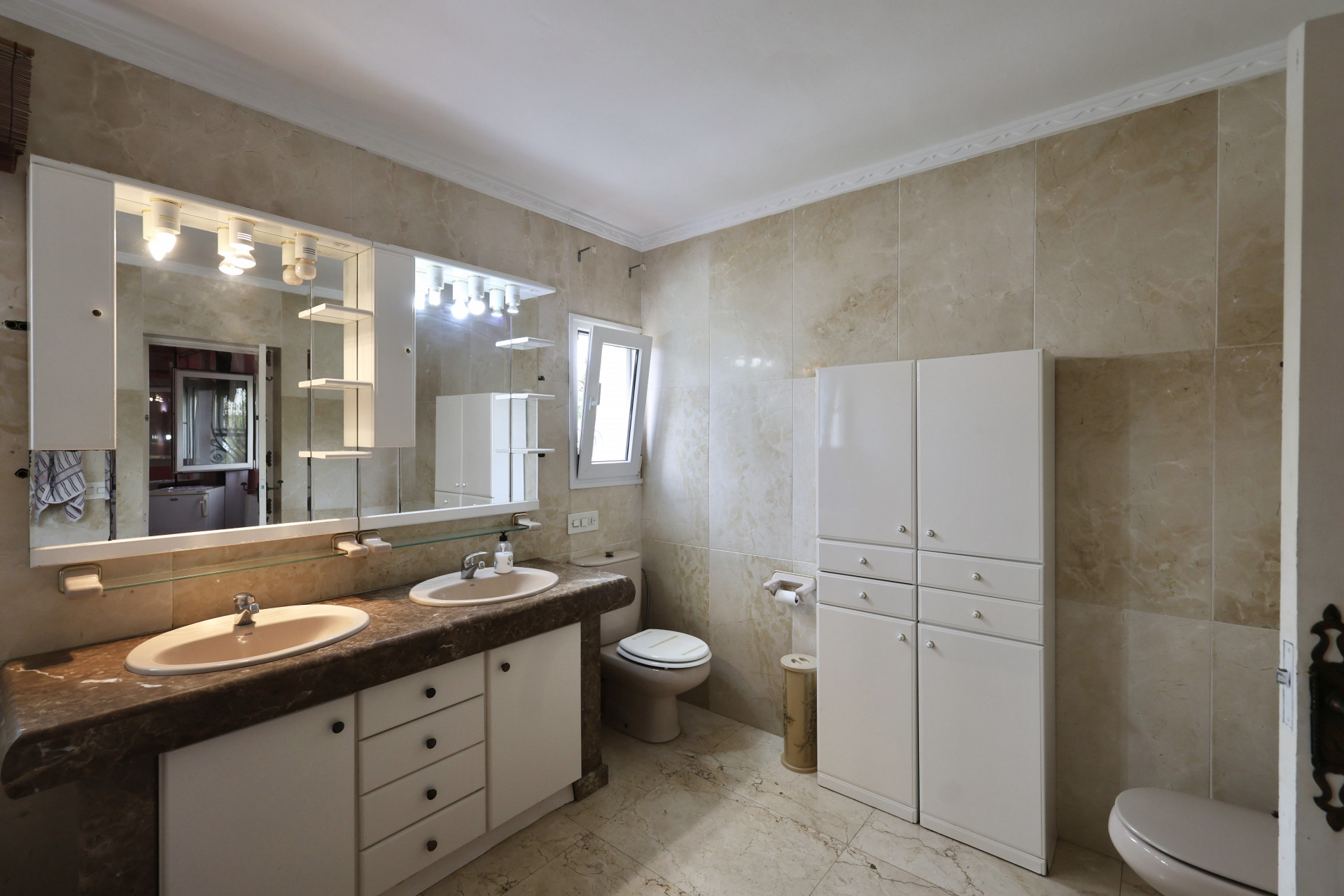 Badkamer met dubbele wastafel, marmeren blad en witte kasten.