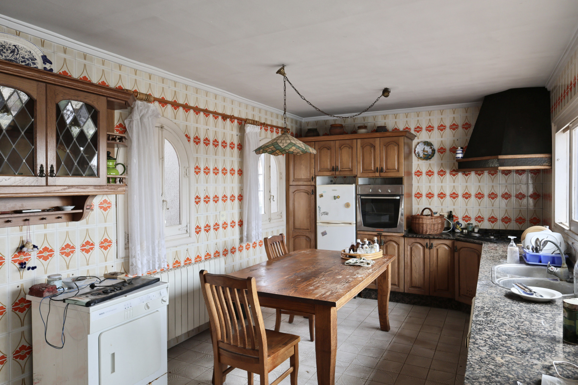 Keuken met tegelmotief en houten meubels, aan renovatie toe.