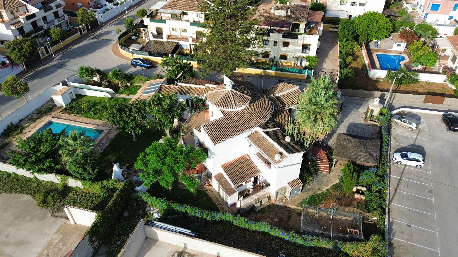 Luchtfoto van de villa met pannendak, zwembad omgeven door groen en aangrenzende parkeerplaats.