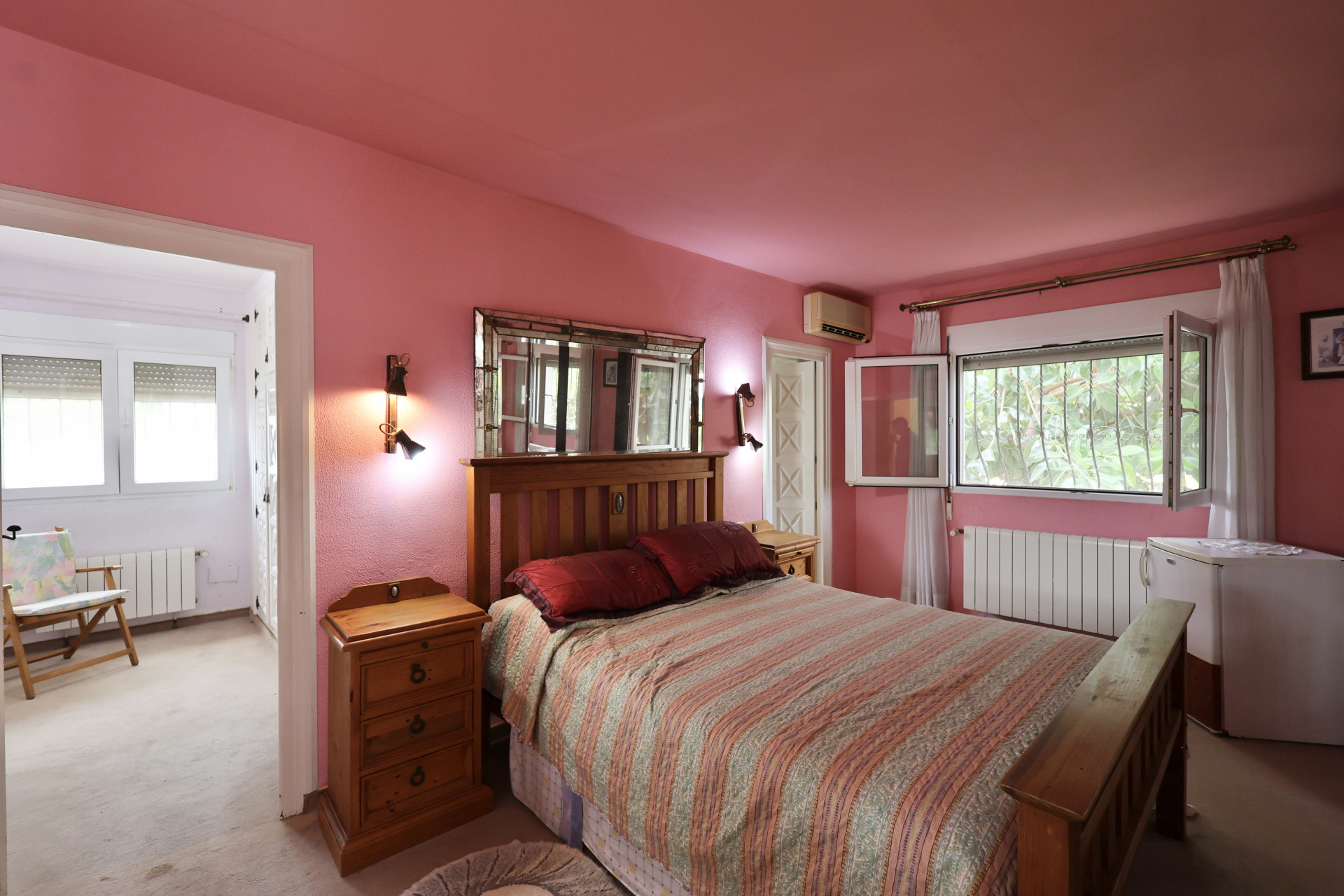 Slaapkamer met roze muren, houten bed en spiegel met lampen. Renovatie nodig.