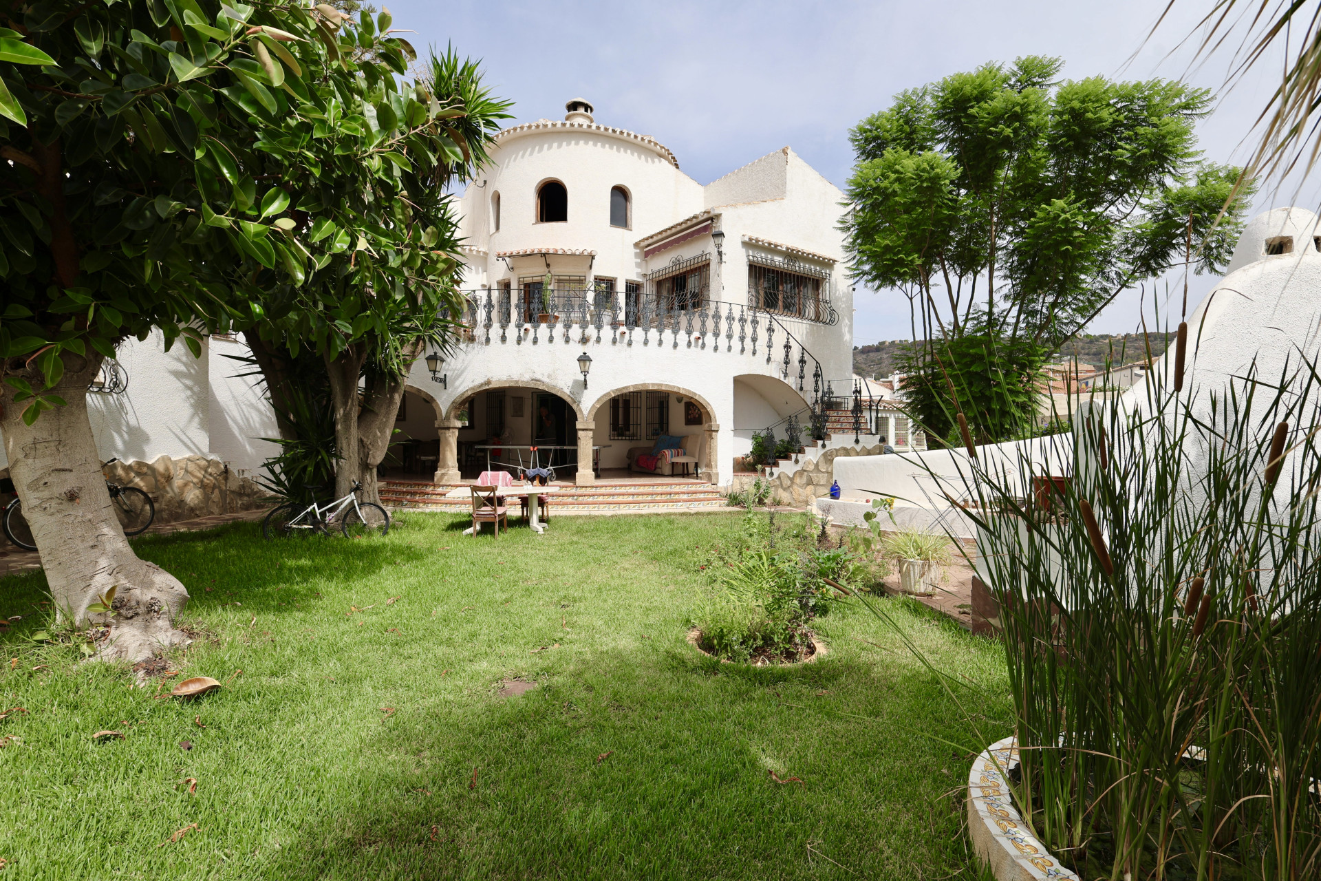 Uitzicht op de voortuin met gazon, groen en de witte gevel van de villa in Javea.