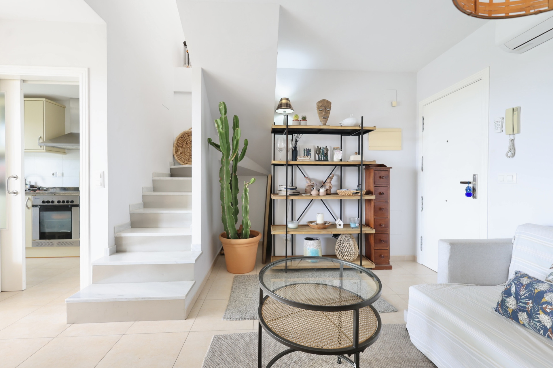 Licht interieur met witte trap, houten en metalen rek, en een rotan salontafel.