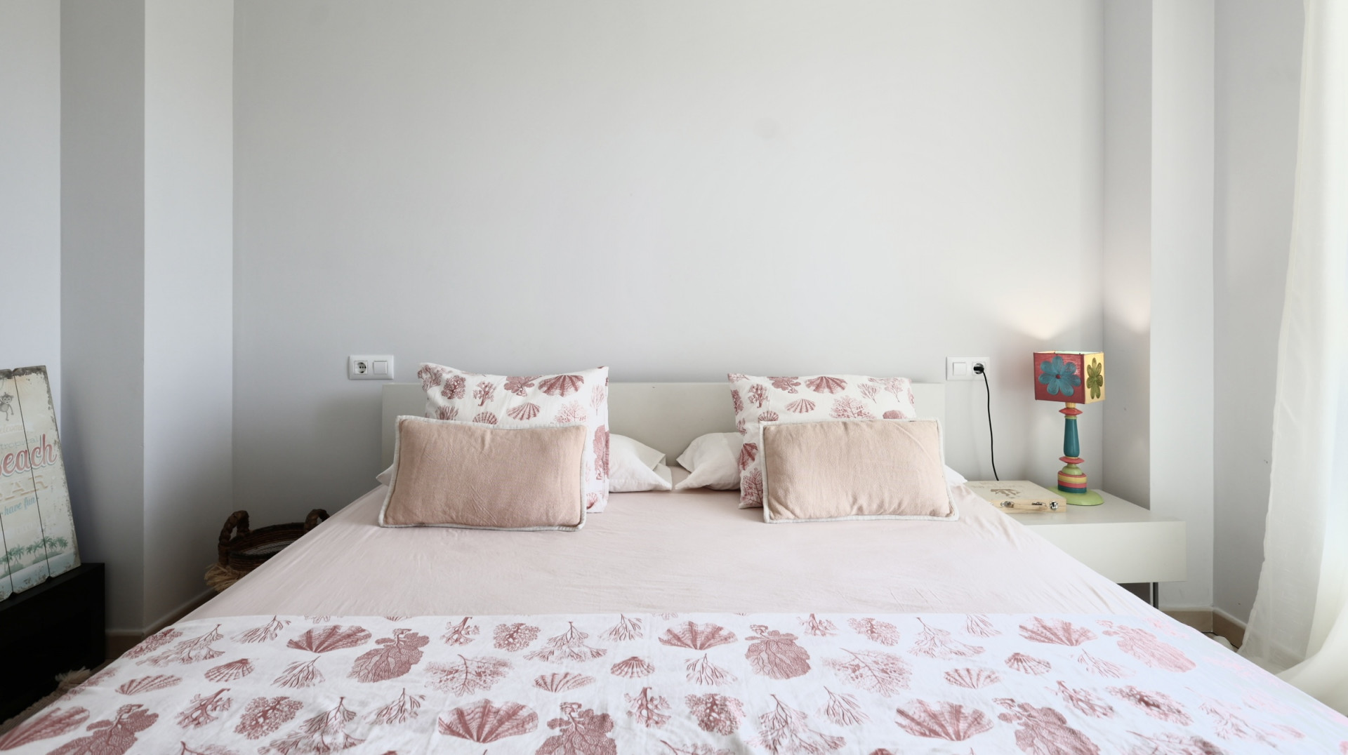 Lichte slaapkamer met een tweepersoonsbed, beddengoed met maritieme motieven en een wit nachtkastje met decoratieve lamp.