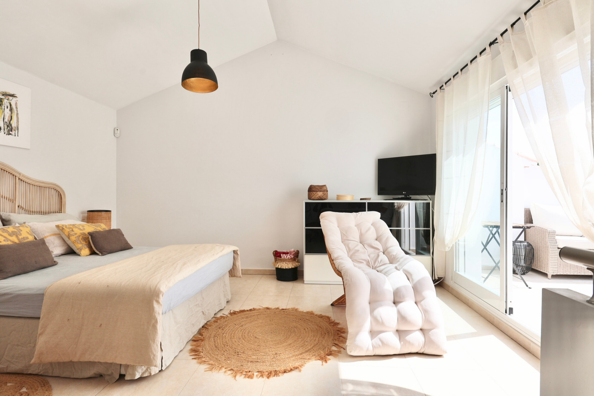 Lichte slaapkamer met rotan bed, jute vloerkleed en toegang tot het terras.