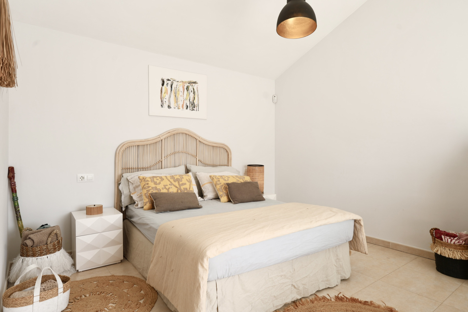 Lichte slaapkamer met rotan bed, rond jute vloerkleed en minimalistische inrichting.