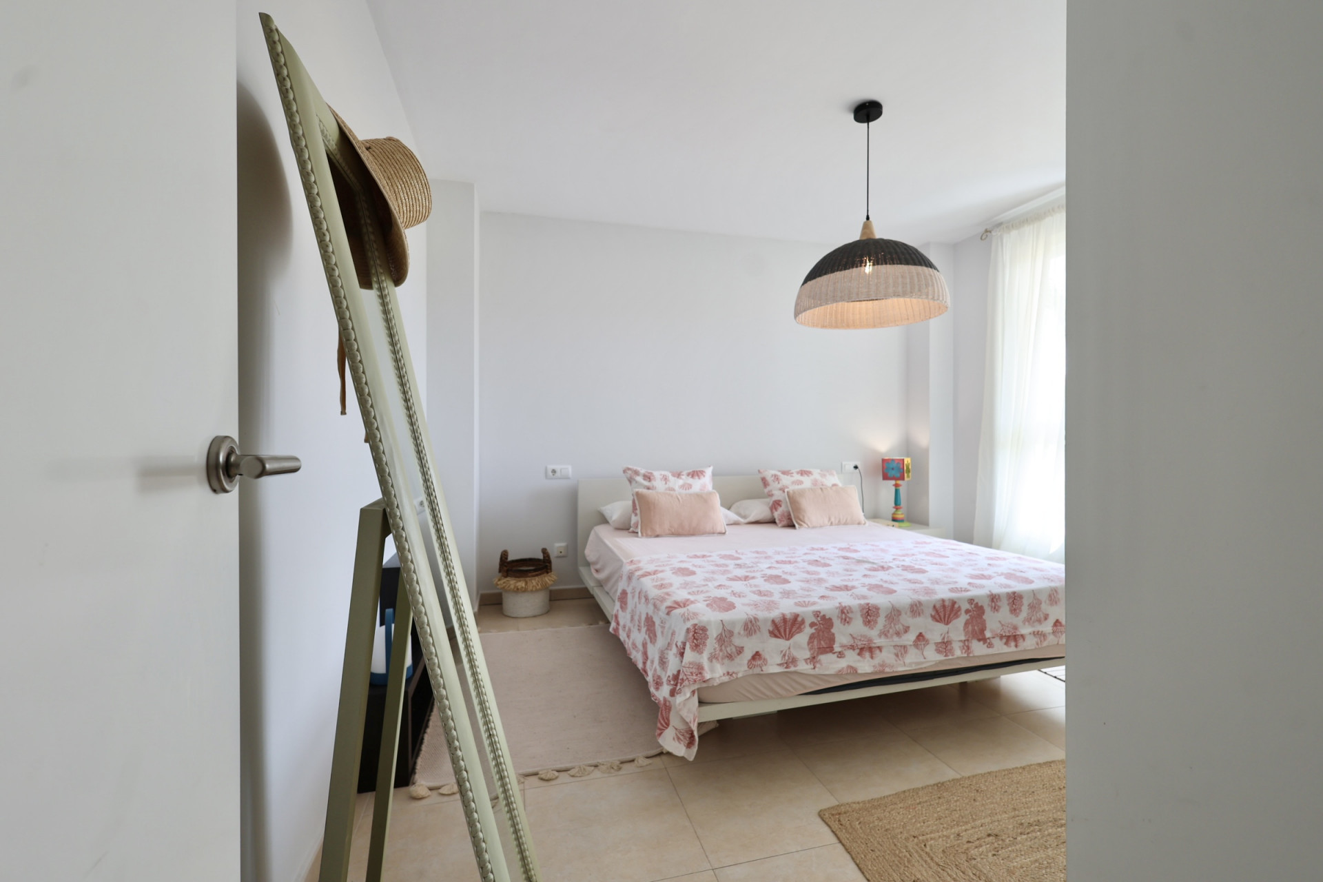 Lichte slaapkamer met tweepersoonsbed, beddengoed met maritieme motieven en een hanglamp van wicker.