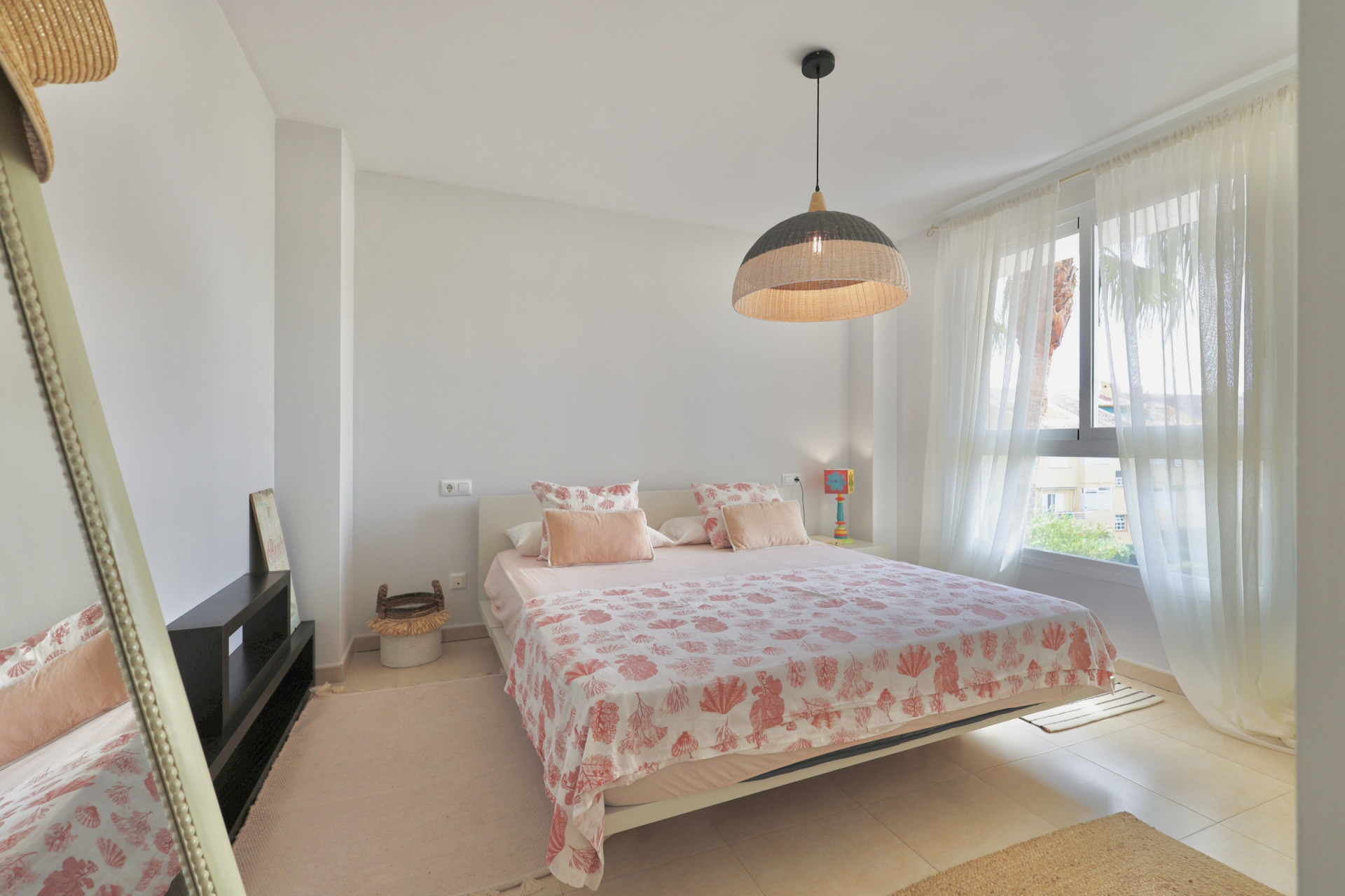 Lichte slaapkamer met tweepersoonsbed, beddengoed met patroon en een hanglamp van wicker.