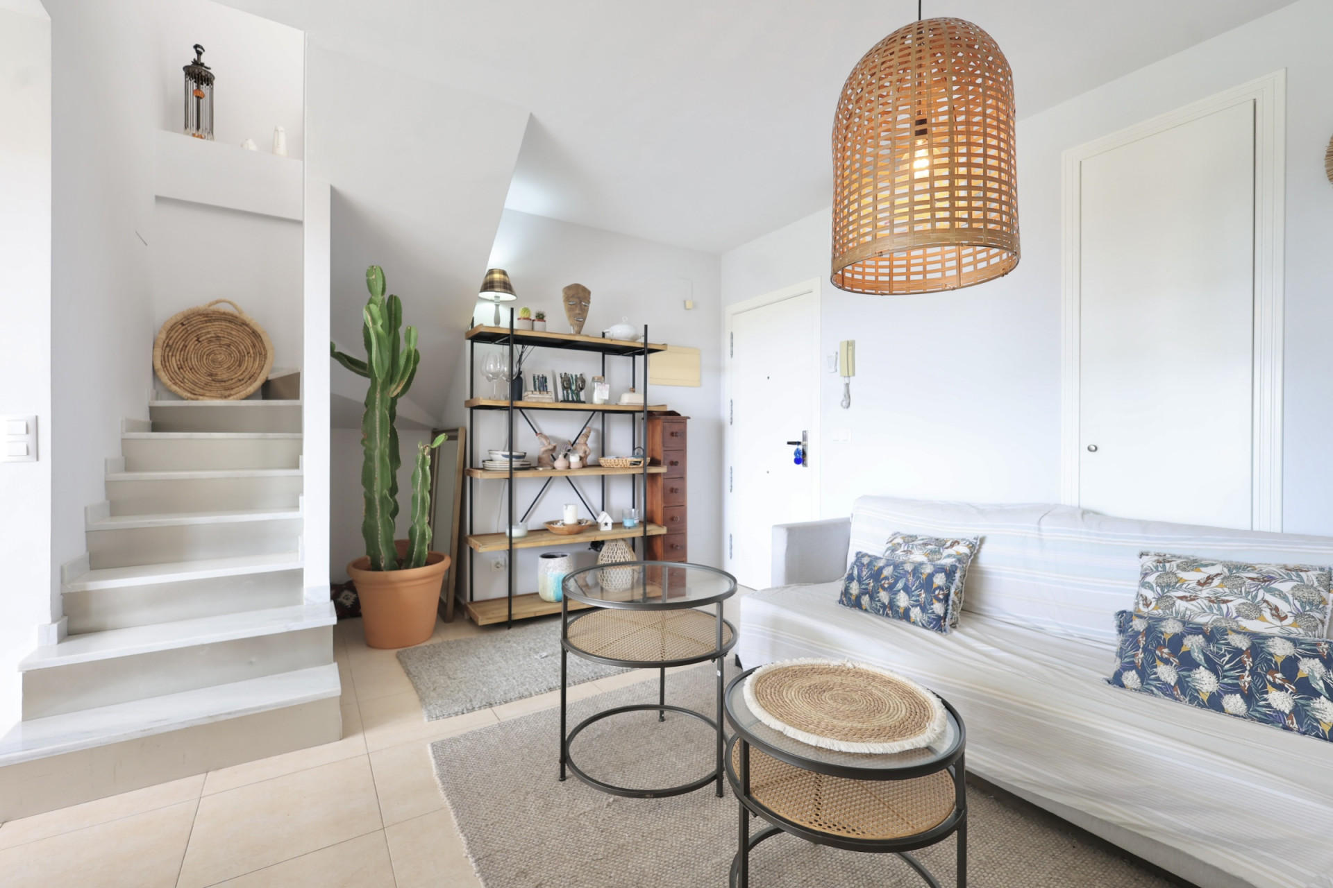 Lichte woonkamer met trap naar de duplex, minimalistische inrichting en een hanglamp van wicker.