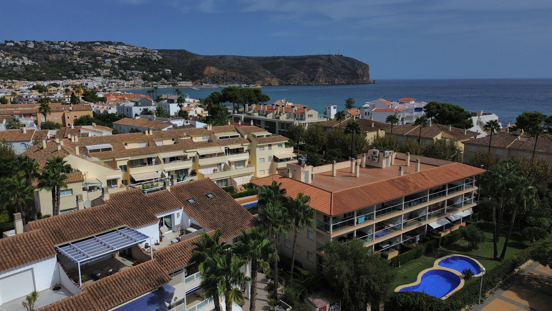 Luchtfoto van de urbanisatie met zwembad en woongebouwen met rode daken nabij de kust van Jávea.