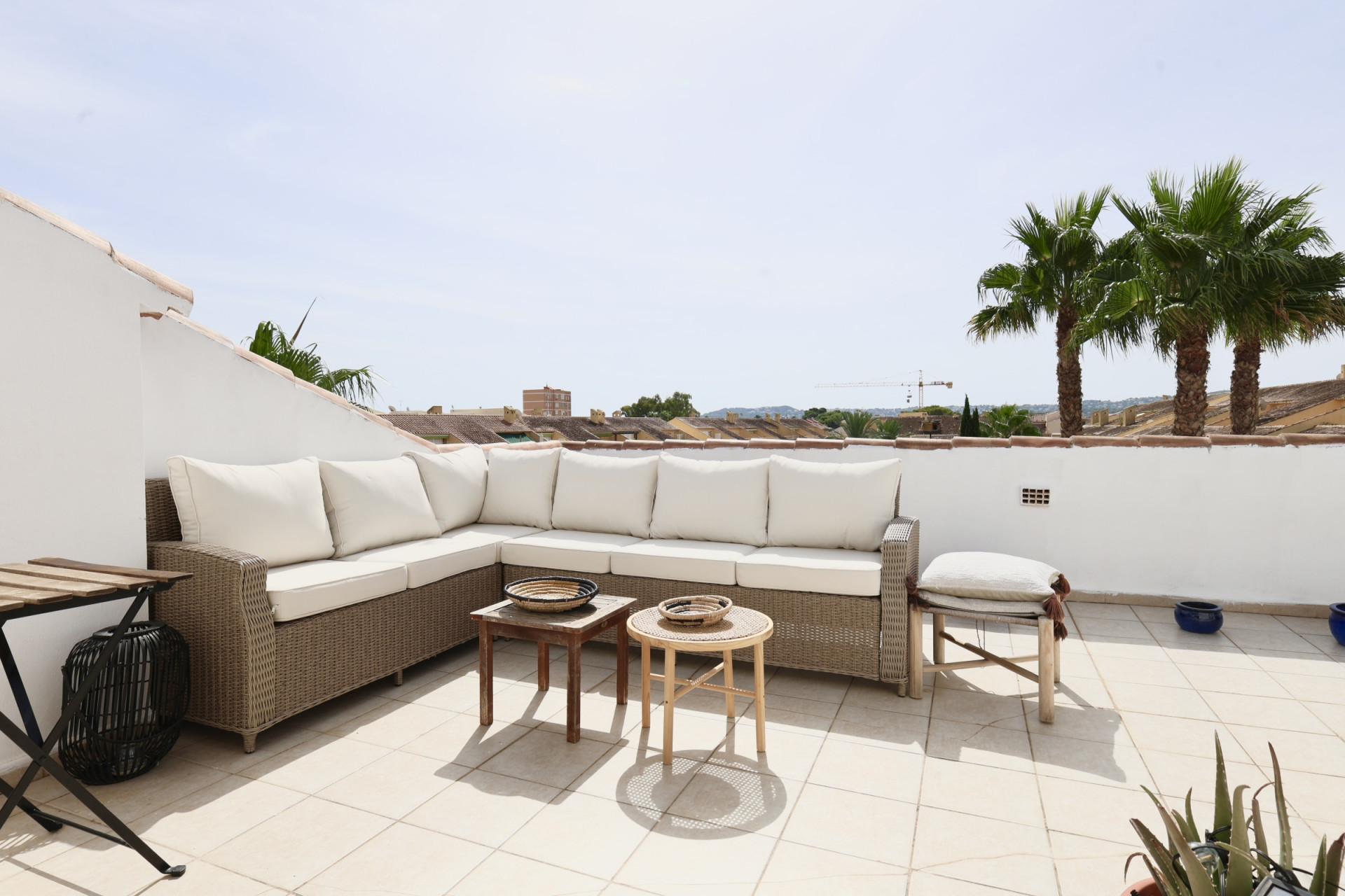 Terras met een wicker hoekbank en witte kussens, met uitzicht op palmbomen en daken.