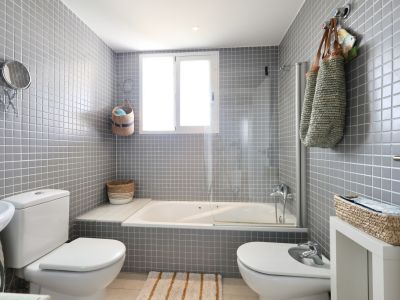Badkamer met grijze tegelwanden, een ligbad met glazen scherm en decoratieve elementen van wicker.