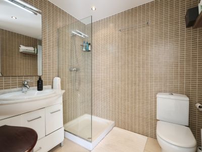 Badkamer met zandkleurige tegelwanden, een glazen douchecabine en een wastafel met marmeren blad.