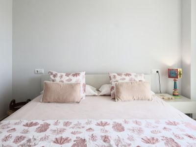 Lichte slaapkamer met een tweepersoonsbed, beddengoed met maritieme motieven en een wit nachtkastje met decoratieve lamp.