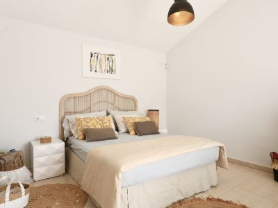 Lichte slaapkamer met rotan bed, rond jute vloerkleed en minimalistische inrichting.
