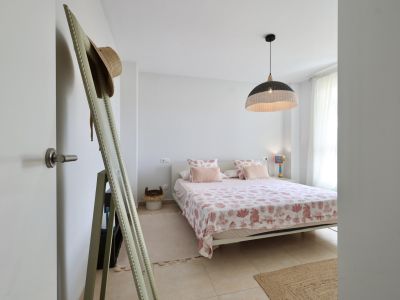Lichte slaapkamer met tweepersoonsbed, beddengoed met maritieme motieven en een hanglamp van wicker.
