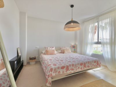 Lichte slaapkamer met tweepersoonsbed, beddengoed met patroon en een hanglamp van wicker.