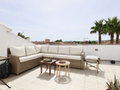 Terras met een wicker hoekbank en witte kussens, met uitzicht op palmbomen en daken.