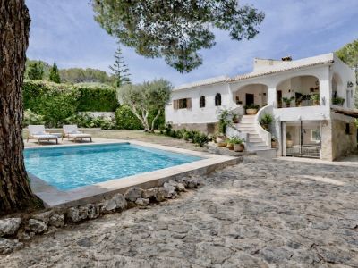Exterieur van een traditionele witte villa met privézwembad, geplaveid terras en buitentrap. Omgeven door een weelderige mediterrane tuin.