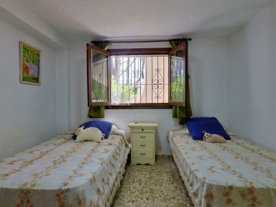 Tweepersoonskamer met twee eenpersoonsbedden, nachtkastje, terrazzovloer en raam met veiligheidsroosters en groen uitzicht.