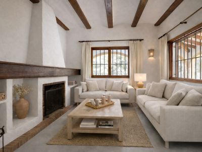 Woonkamer met traditionele witte stucwerk open haard en donkere houten schouw. Zichtbare plafondbalken en houten ramen met tralies kenmerken de ruimte.