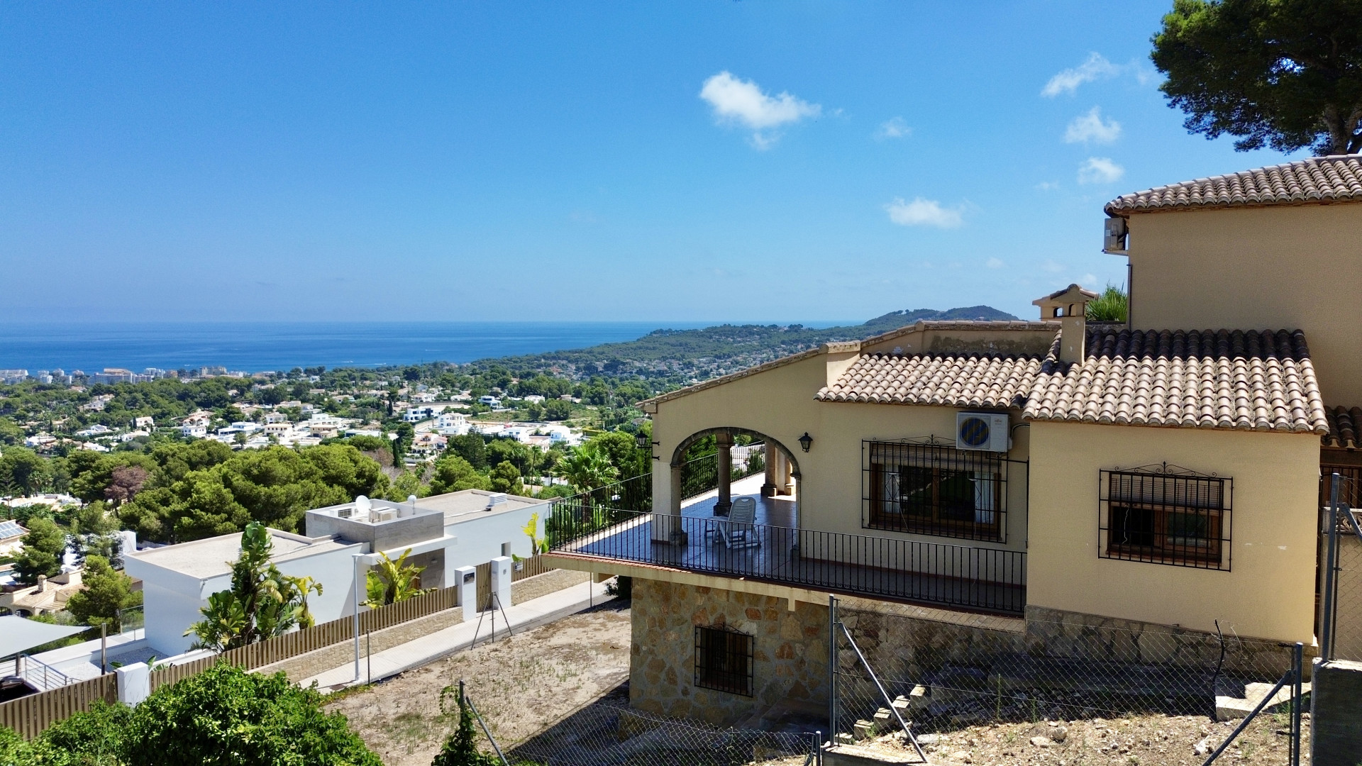 Exterieur van de villa met overdekt terras, boogontwerp en zwarte balustrades. Het hellende perceel biedt panoramisch uitzicht op de zee, de stad en de bergen.