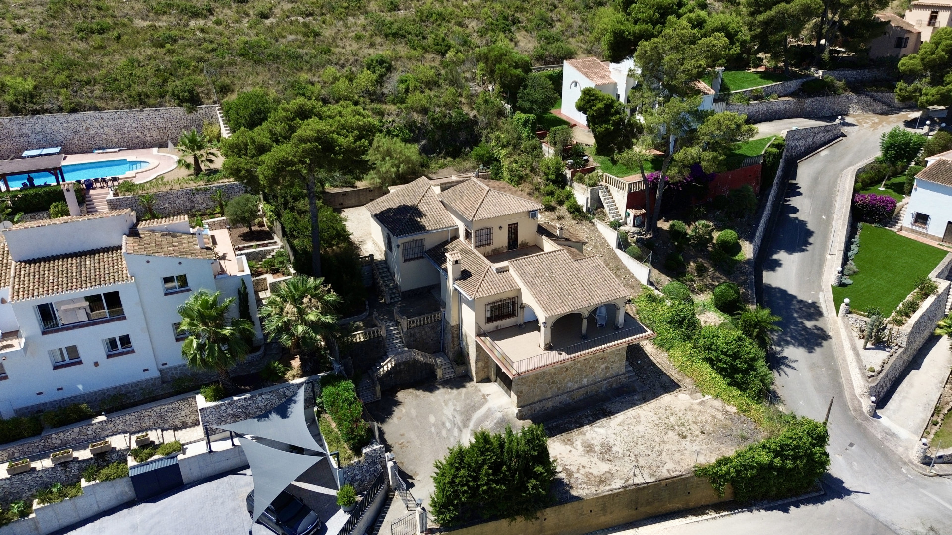 Luchtfoto van de villa met meerdere verdiepingen, traditionele pannendaken, diverse terrassen en hellende tuinen, omgeven door mediterrane begroeiing.