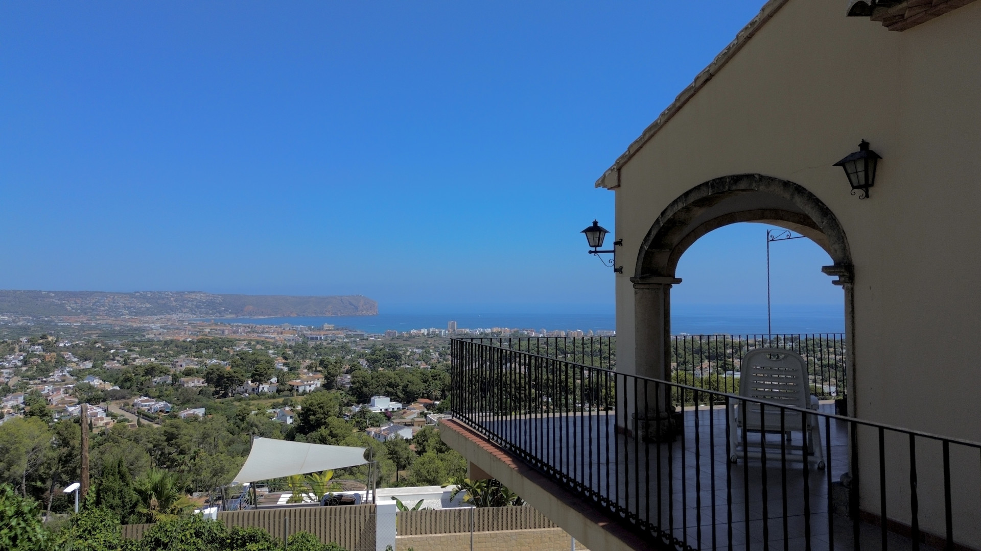 Overdekt terras met panoramisch zee-, stads- en landschapszicht, omlijst door een stenen boog en smeedijzeren balustrade.