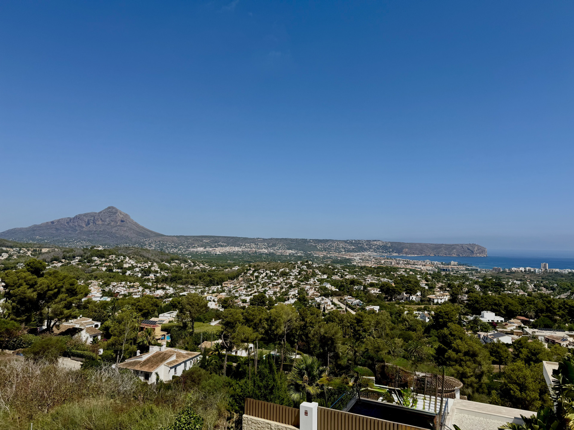 Panoramisch uitzicht op Jávea met de imposante Montgó, de Middellandse Zee en het groene, beboste stadslandschap onder een heldere lucht.