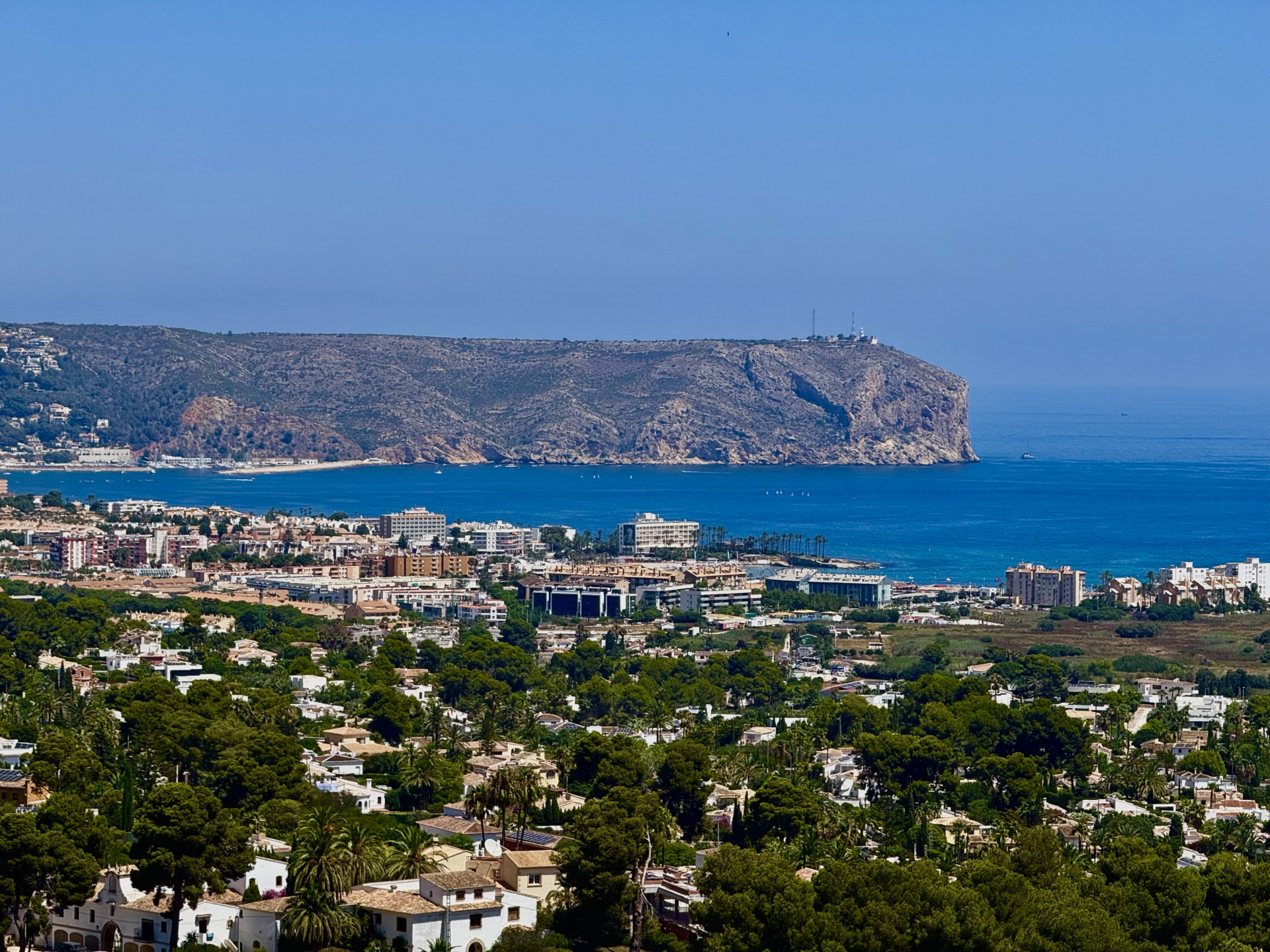 Uitgestrekt panoramisch uitzicht op het woonlandschap van Jávea, de diepblauwe Middellandse Zee met boten en de prominente rotskaap met zijn vuurtoren.