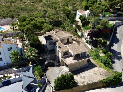 Luchtfoto van de villa met meerdere verdiepingen, traditionele pannendaken, diverse terrassen en hellende tuinen, omgeven door mediterrane begroeiing.