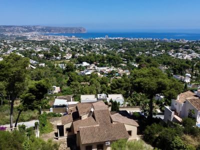 Luchtfoto van Jávea, met traditionele villa's met terracotta daken tussen pijnbomen, en de Middellandse Zee en Cabo de San Antonio op de achtergrond.