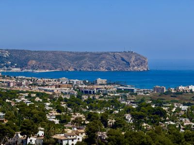 Uitgestrekt panoramisch uitzicht op het woonlandschap van Jávea, de diepblauwe Middellandse Zee met boten en de prominente rotskaap met zijn vuurtoren.
