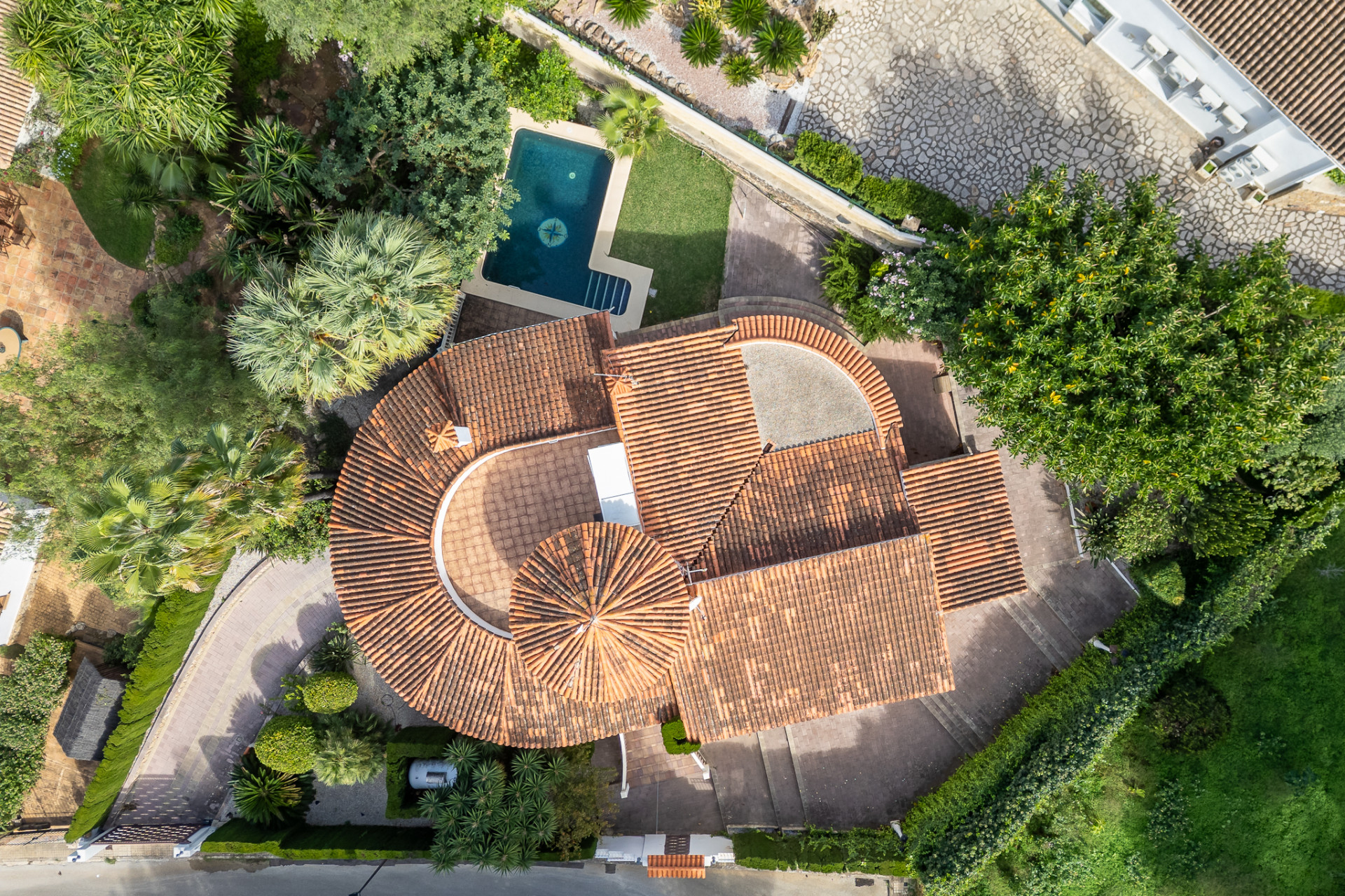 Luchtfoto van de villa met kenmerkende rode pannendaken, privézwembad met kompasontwerp en weelderige mediterrane tuinen.