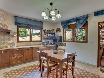 Functionele keuken met donkerhouten kasten, decoratieve tegelwand en een vloer met patroontegels. Twee ramen bieden uitzicht op de tuin, compleet met een houten eettafel.