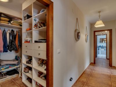 Gang met geïntegreerde open kledingkast, witte planken en lades, terracotta vloertegels en houten deurkozijnen.