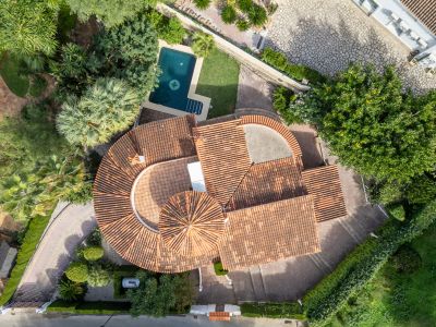 Luchtfoto van de villa met kenmerkende rode pannendaken, privézwembad met kompasontwerp en weelderige mediterrane tuinen.