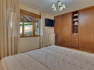 Slaapkamer met tweepersoonsbed, ingebouwde houten kasten en raam met uitzicht op een aangelegde muur. Voorzien van een wand-tv en witte ladekast.