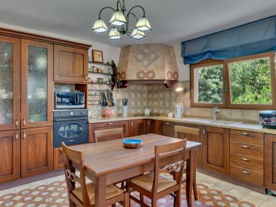 Traditionele keuken met donkerhouten kasten, een betegelde achterwand met patronen en een centrale eettafel. Natuurlijk licht stroomt binnen via het raam met uitzicht op groen.