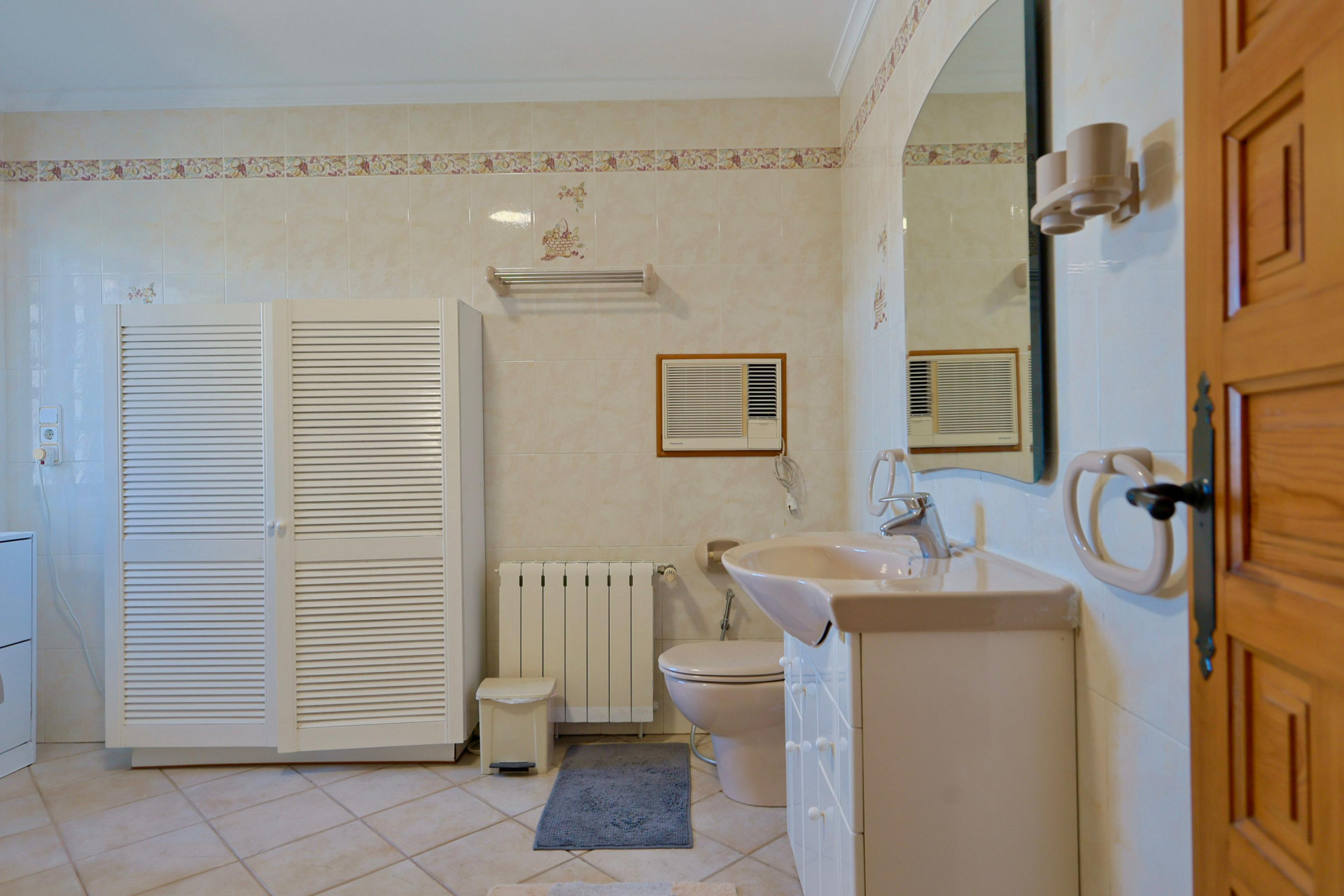 Betegelde badkamer met witte kast met lamellen en een beige wastafel.