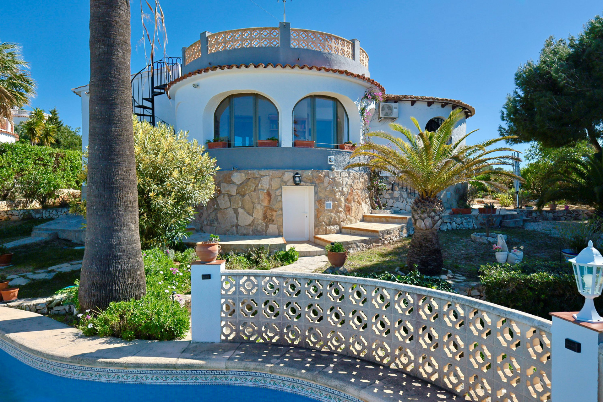 Buitenaanzicht van de villa met zwembad en stenen gevel, omgeven door mediterrane tuinen.