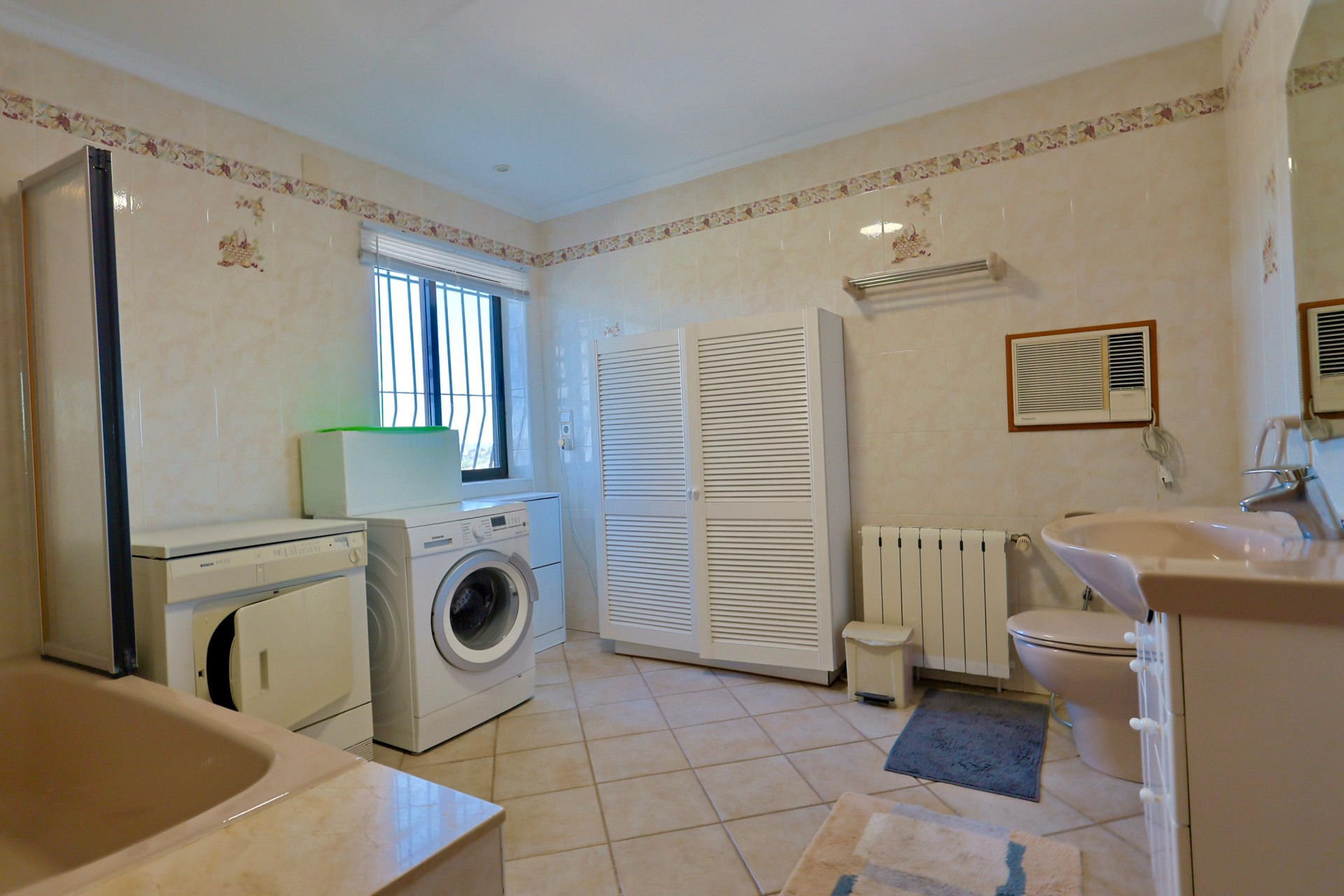 Functionele badkamer met wasmachine, droger en ruime witte kast met lamellen.