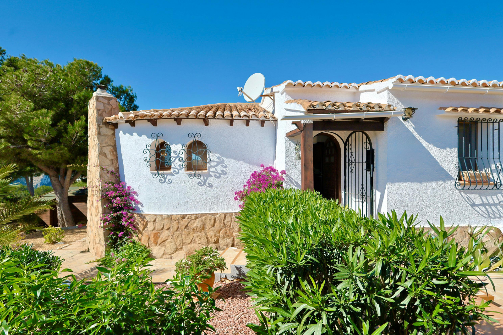 Gevel van een mediterrane villa met stenen details, dakpannen en sierlijk smeedwerk.