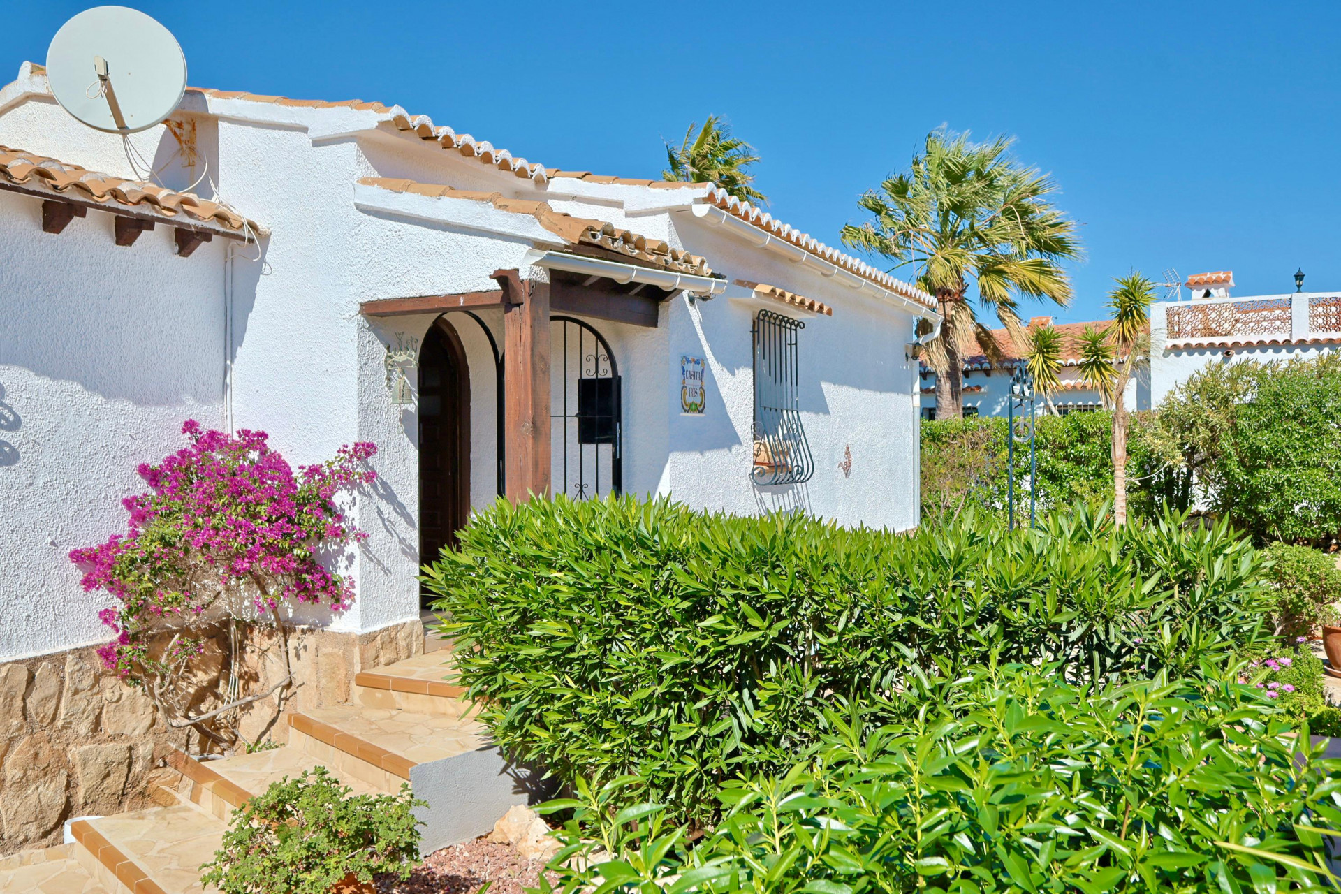 Gevel van mediterrane villa met bougainville en houten boogingang.