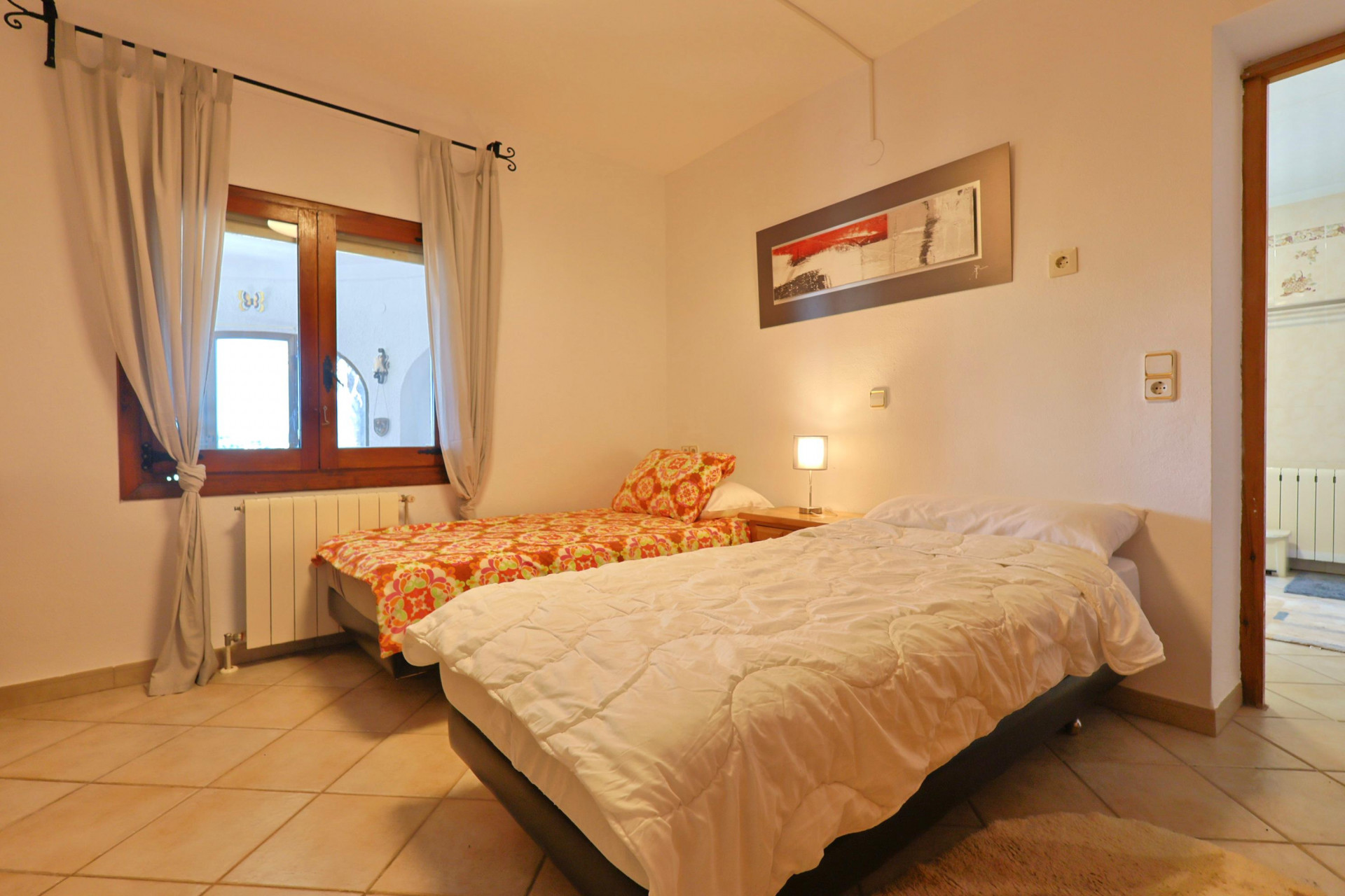 Lichte slaapkamer met twee eenpersoonsbedden, een houten raamkozijn en een tegelvloer.