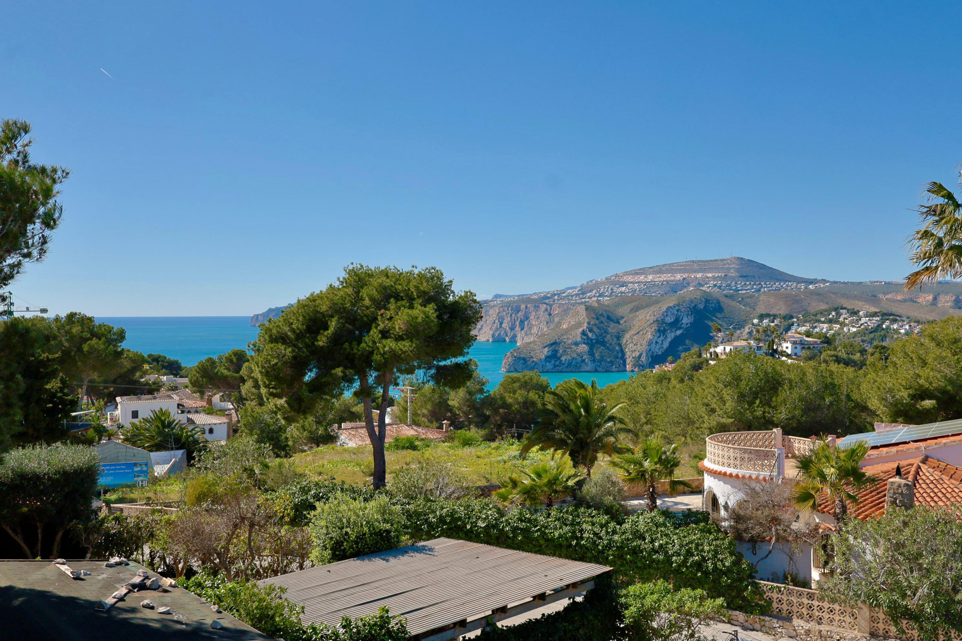 Panoramisch uitzicht op de kust en bergen van Jávea vanaf het terras, met mediterrane vegetatie.